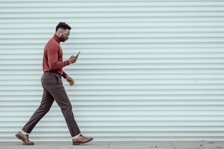 Portrait of African-American young businessman using smartphone while walking