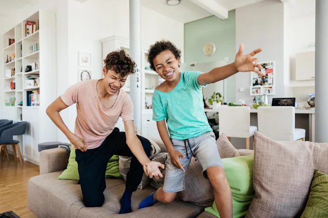 Two brothers messing around, standing on the couch playing and having fun together at home.