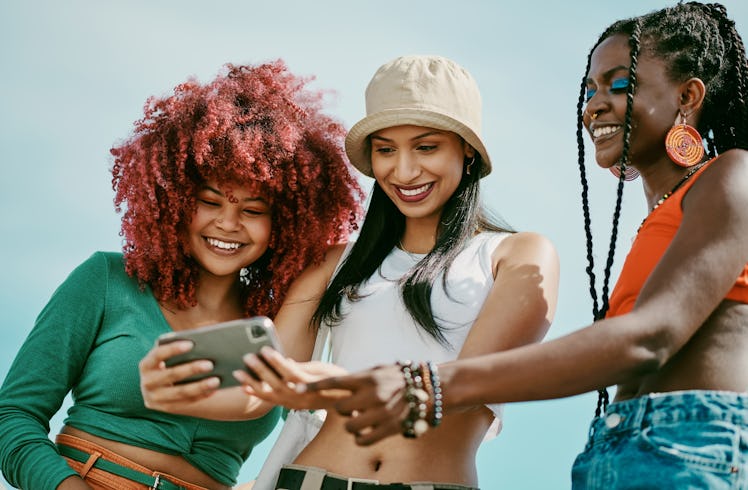 three young women smile at a cell phone as they read about how their zodiac signs will be the luckie...