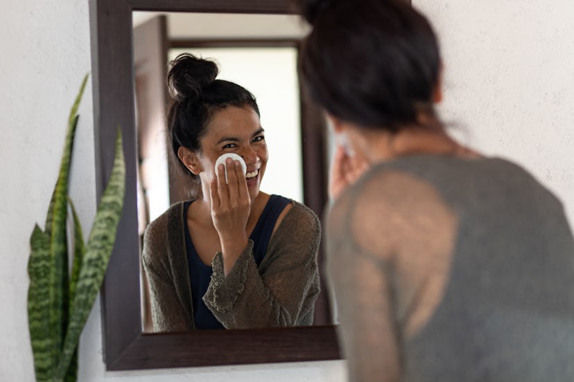 Woman cleansing face looking into bathroom mirror