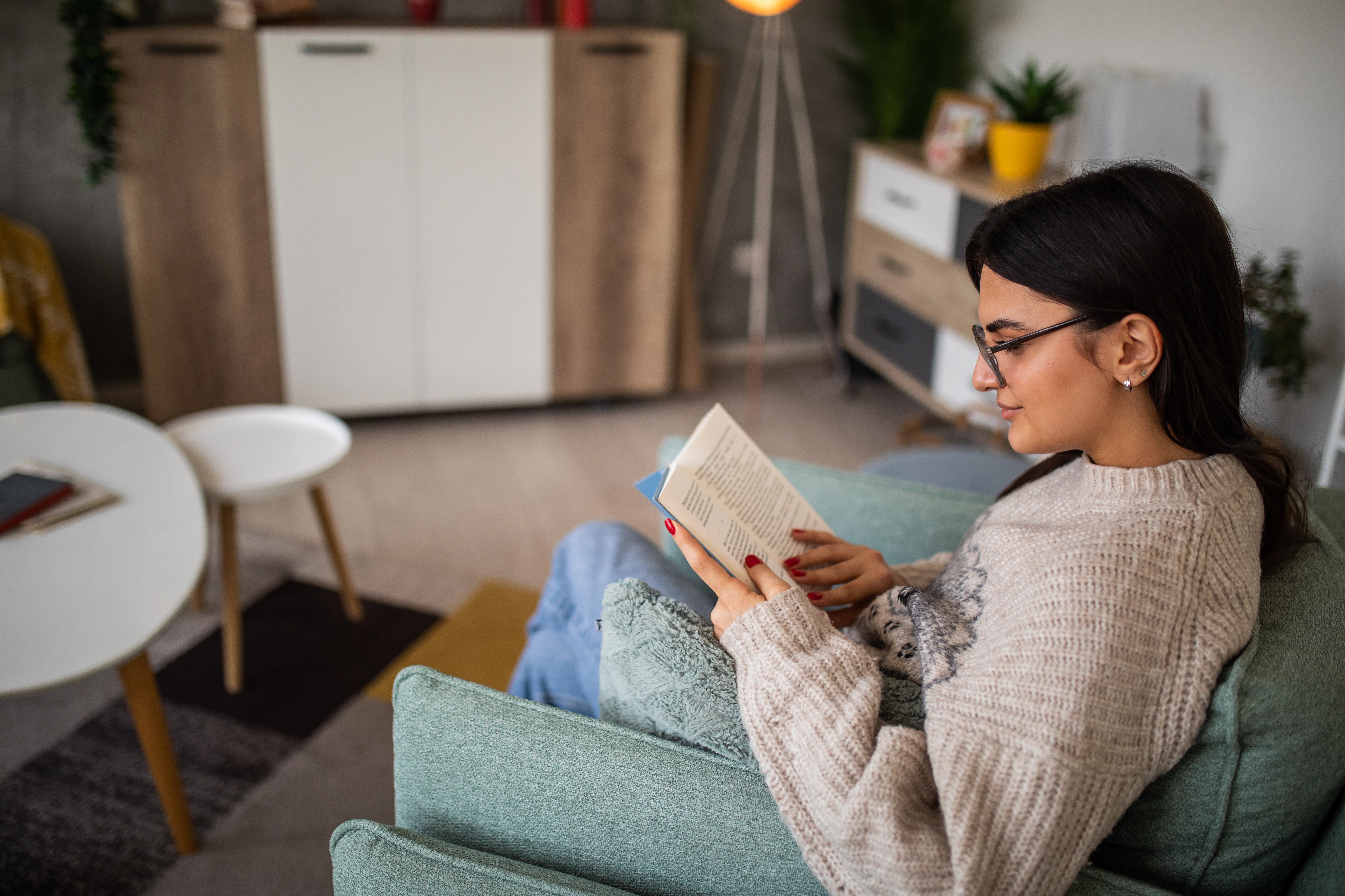 Young woman reading a book in an armchair at home