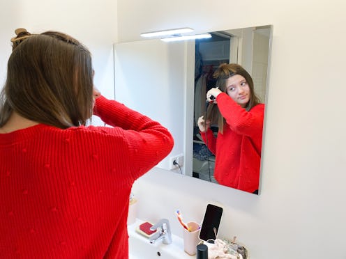 Beautiful teenage girl ironing her hair in the bathroom