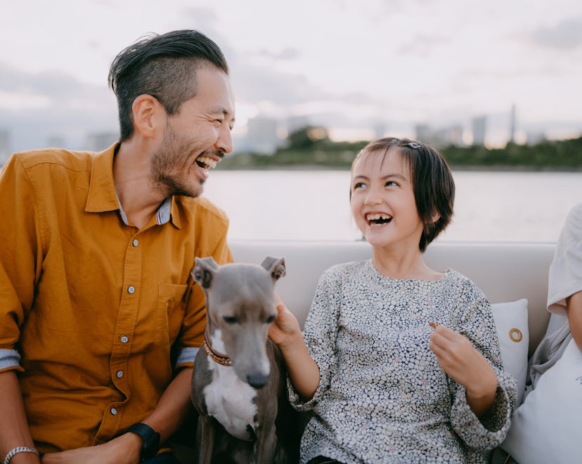 Father and young daughter laughing with a dog, in a list of April Fools pranks for dogs