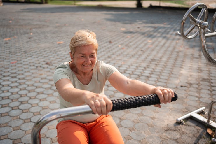 Active senior woman is exercising on a machine in an outdoor gym.