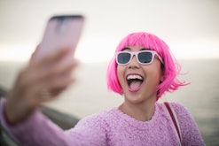 happy young woman in pink wig and sunglasses taking a selfie by the water in roundup of aries captio...