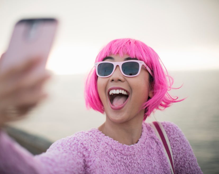happy young woman in pink wig and sunglasses taking a selfie by the water in roundup of aries captio...