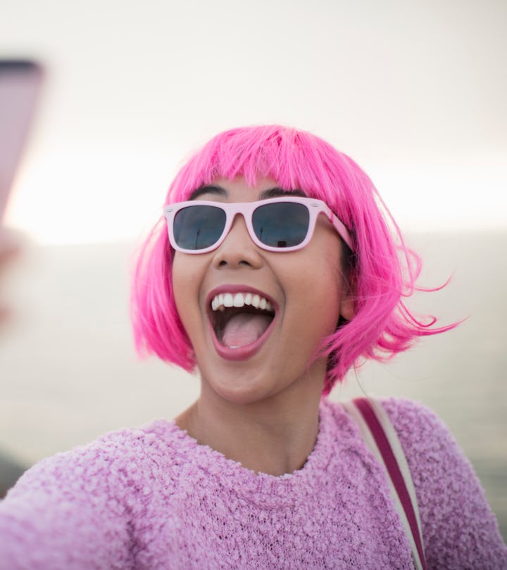 happy young woman in pink wig and sunglasses taking a selfie by the water in roundup of aries captio...