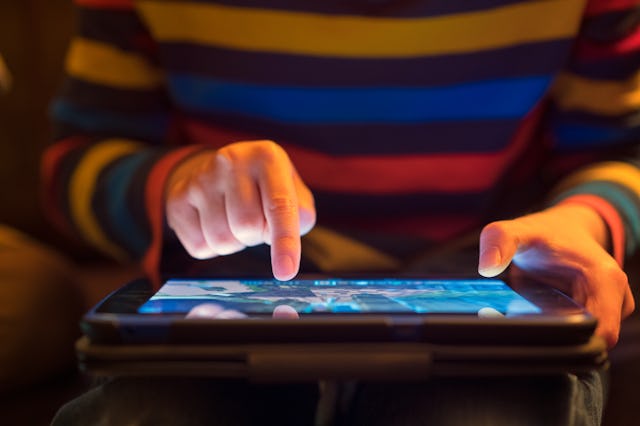Close up of a young boy using a tablet computer, his finger hovering over it as he's about to touch ...