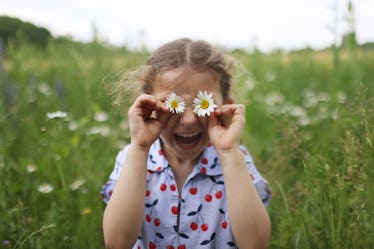 A child holding flowers up to her eyes, the simplest form of a spring joke for kids.