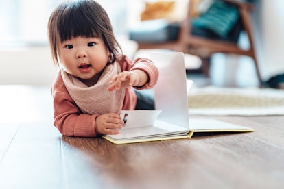 Baby girl turning the page while reading a book, lying down on the floor at home, in a story about b...