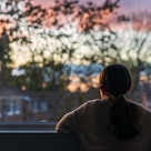 A young kid looks out of their dark bedroom window. 