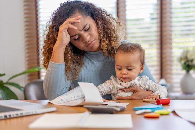 Mother and her baby sitting at the table with a laptop. Mother is working on the document. She looke...