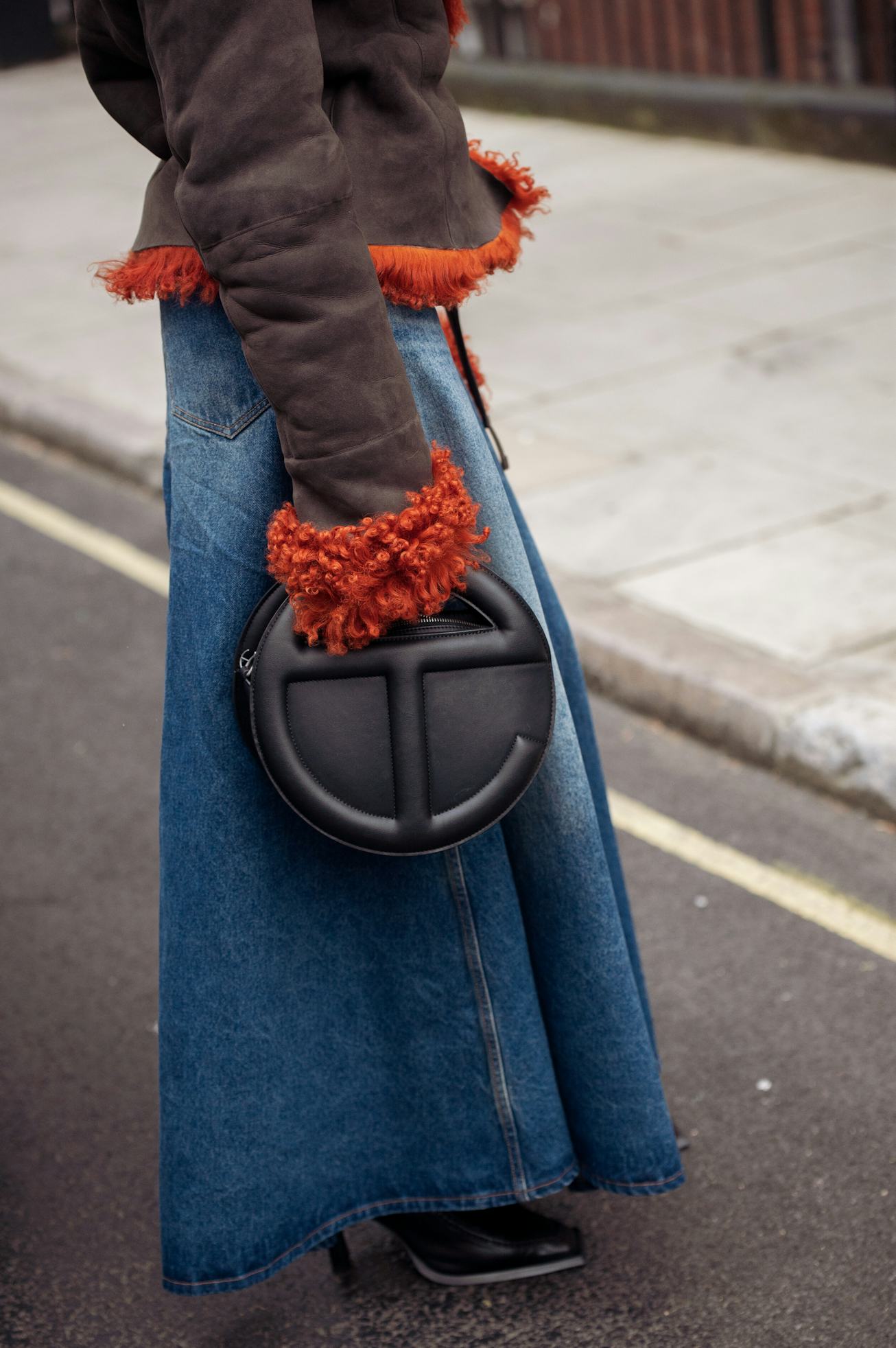LONDON, ENGLAND - FEBRUARY 18: A guest wearing a long denim skirt, dark brown aviator jacket with or...