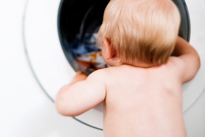 A baby looking into a washing machine which, at some point, will have a diaper in it.