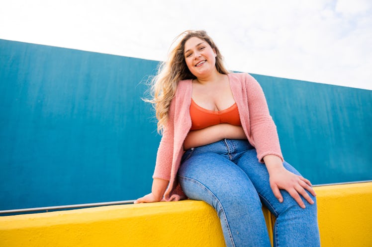 young woman poses on a bright yellow wall as she considers how she’ll be affected by the april 2023 ...