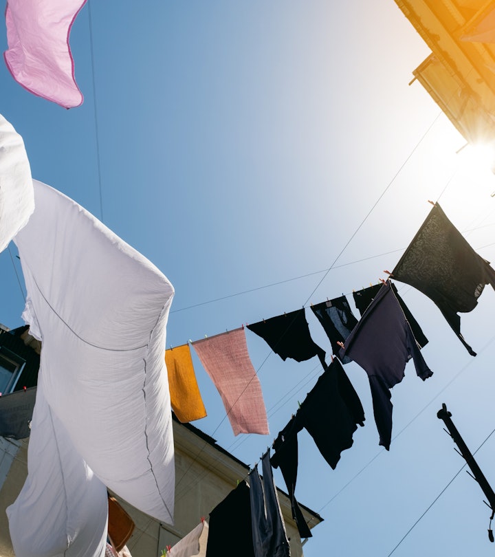 Clean sweaters, trousers and T-shirts hang on a rope outside on a sunny summer day, against a blue s...