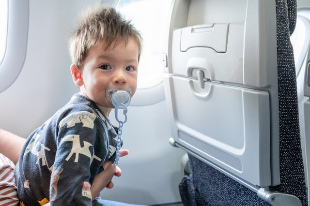 baby boy traveling in airplane flying sitting on his mother lap and using pacifier in the aircraft.;...