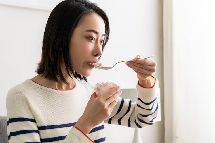 young pretty Asian woman sitting on a cozy sofa in the living room while eating icecream.