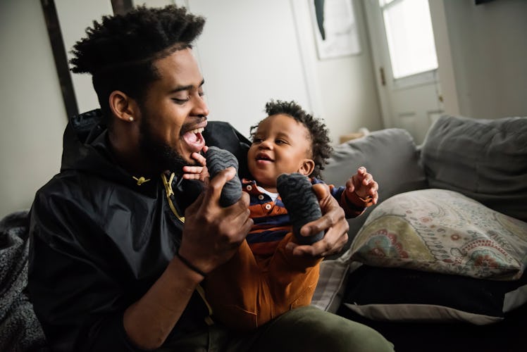 Father dressing baby boy in living room. Dad is in thirties, baby is one year’s old. Horizontal wais...