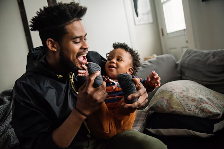 Father dressing baby boy in living room. Dad is in thirties, baby is one year’s old. Horizontal wais...