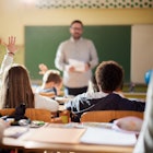 Rear view of schoolgirl raising her hand to answer the teacher's question on a class at elementary s...