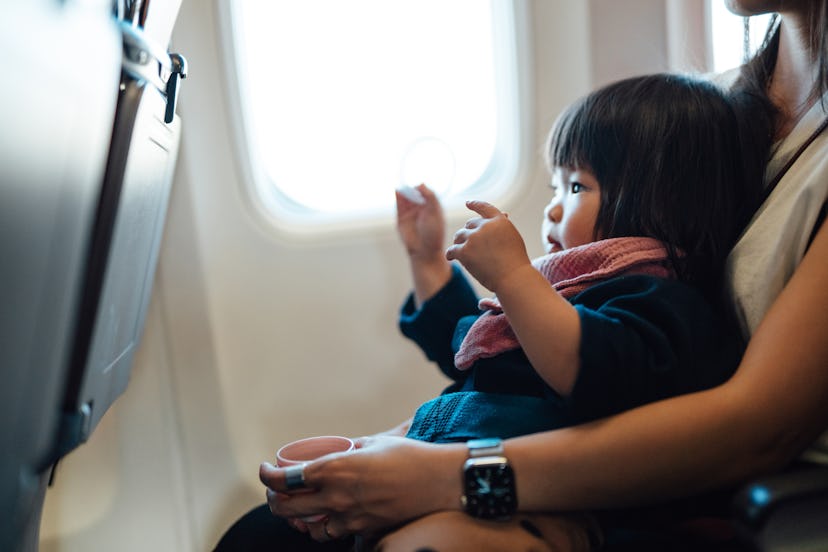 Mother taking airplane with daughter. Toddler traveling in airplane, sitting on her mother lap in th...