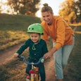 Photo of a young boy who is learning to ride a bicycle with a little help from his mother