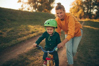 Photo of a young boy who is learning to ride a bicycle with a little help from his mother