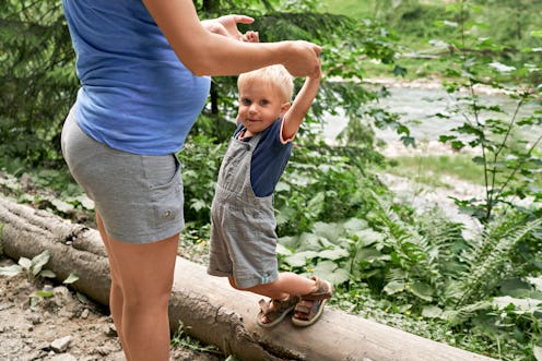 Pregnant woman and her little son play holding hands near the river. Concept of healthy lifestyle