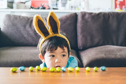 Young boy wearing rabbit eats looking at a line of easter eggs laid out on a table in article about ...