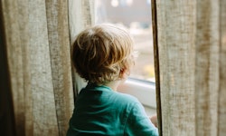 A toddler photographed from the back, between linen curtains. Kids sometimes need advocates outside ...