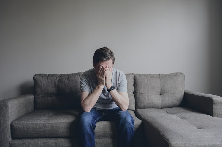 A man sitting on a couch with his head in his hands.
