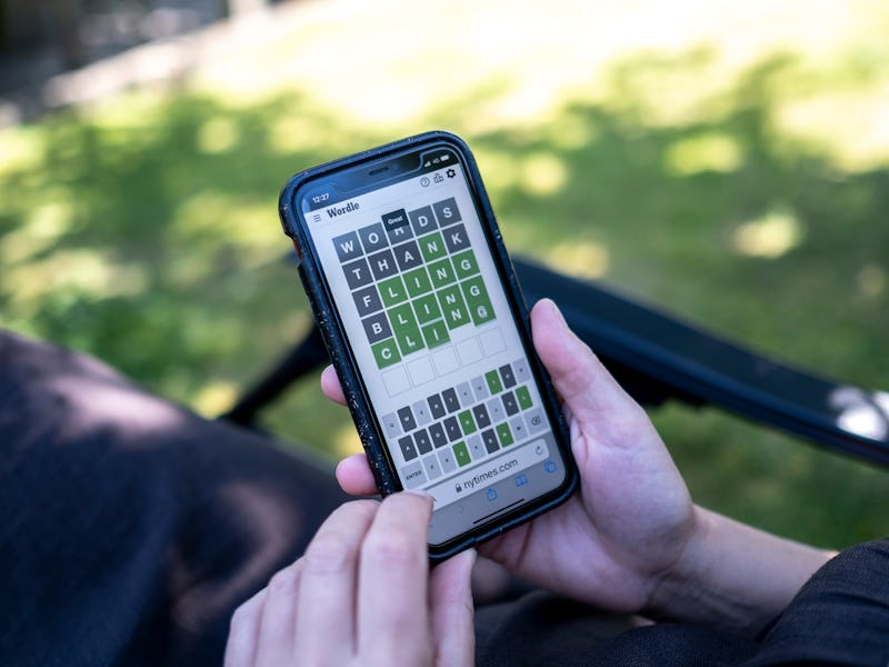 Woman plays Wordle on her smartphone from a seat in a garden and struggling to complete the last wor...