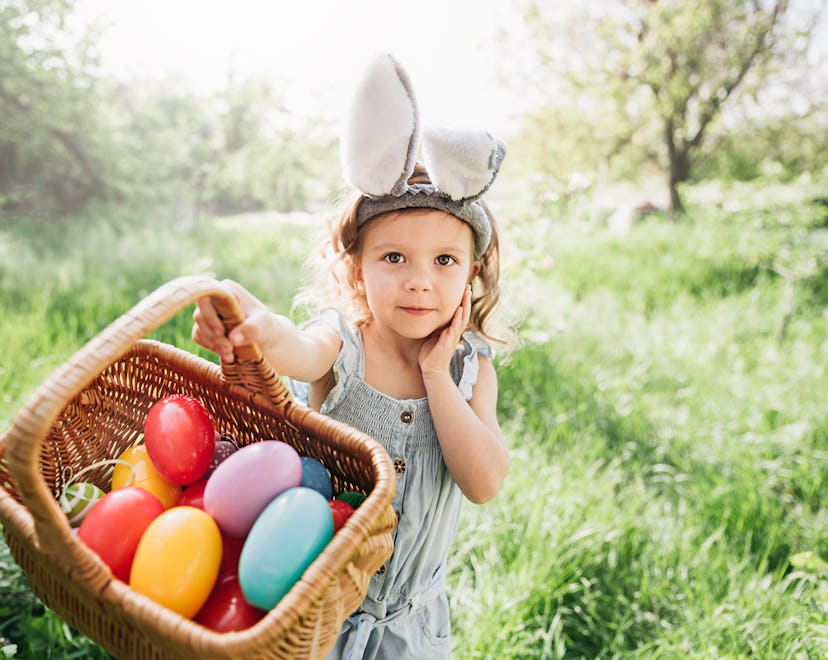 Easter egg hunt for toddlers. Toddler girl Wearing Bunny Ears Running To Pick Up Egg In Garden.