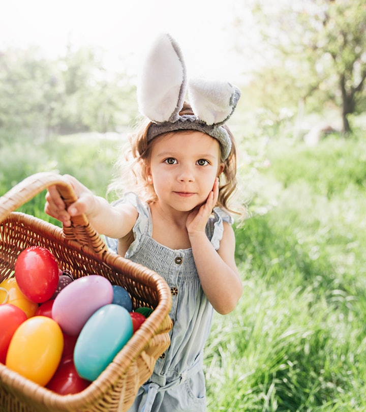 Easter egg hunt for toddlers. Toddler girl Wearing Bunny Ears Running To Pick Up Egg In Garden.
