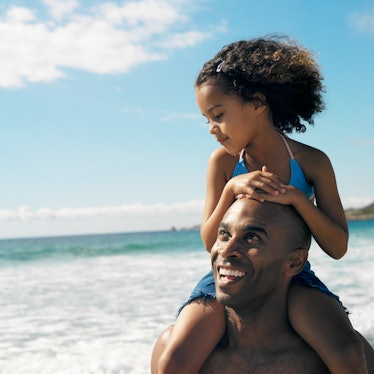 A father smiling with his daughter on his shoulders on a beach