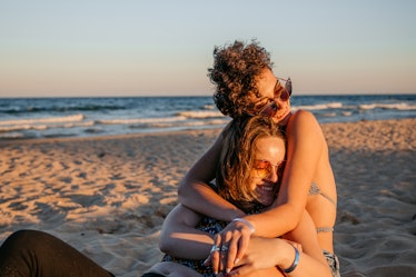 two young women smile and embrace on a beach, as they consider how saturn in pisces will affect thei...