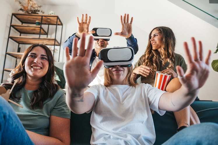 Four friends playing on the Metaverse with Virtual Reality headset from home living room.