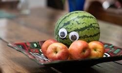 Melon with googly eyes, sitting in a bowl intimidating some apples