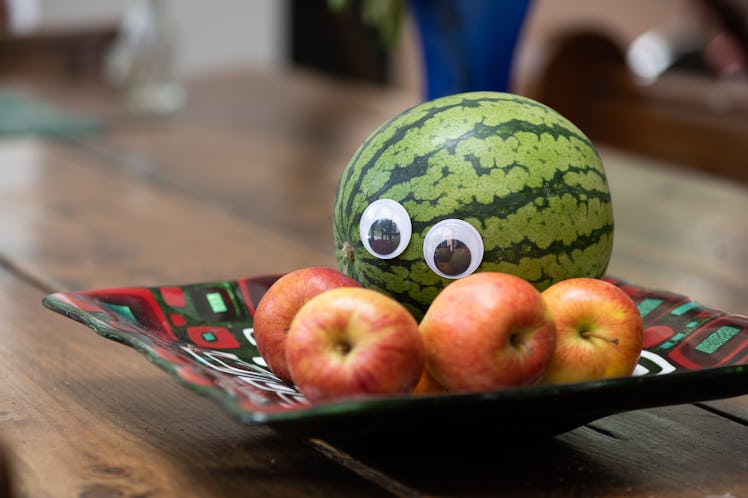 Melon with googly eyes, sitting in a bowl intimidating some apples