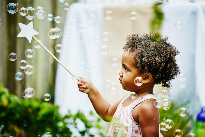 Toddler girl with star wand playing with bubbles in backyard during birthday party
