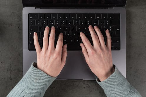 A top down POV view of a caucasian person working on a modern laptop computer at a work desk.