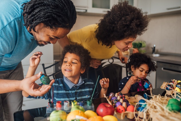 Young couple with two children decorating Easter eggs, having an indoor Easter egg hunt in the rain