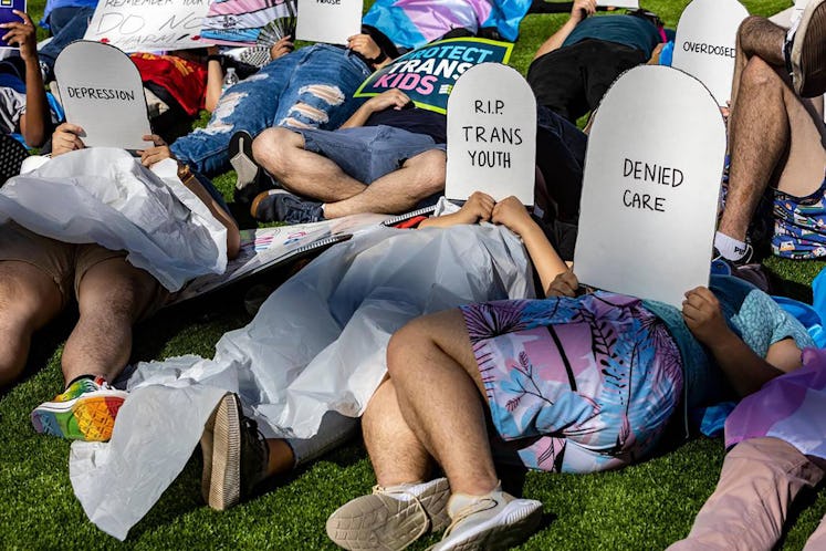Protesters lie on the ground holding cardboard signs shaped like tombstones in front of the Marriott...