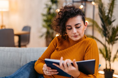 Beautiful young woman reading a book at home at night.