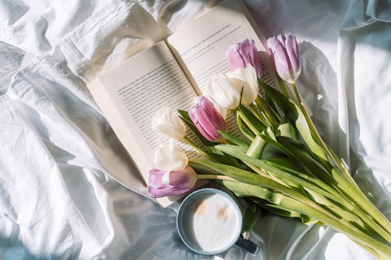 Bouquet of tulips with a book and a cup of coffee on a white bed.