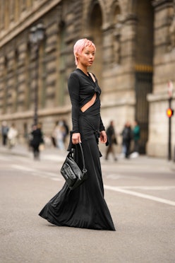 PARIS, FRANCE - MARCH 05: A guest wears a black knot cut-out pattern long sleeves / long dress, a bl...