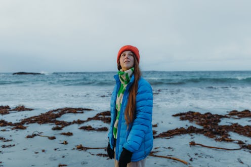 Side view of a female with long hair and inblue jacket walking at the scenic beach with cold ocean v...