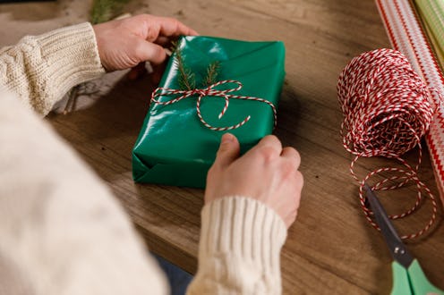 Over the shoulder view of crafty young man typing a red and white twine around a Christmas gift box ...