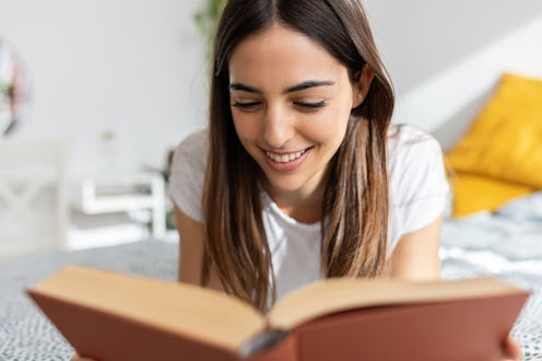 Close-up view of happy young woman reading a book lying on bed